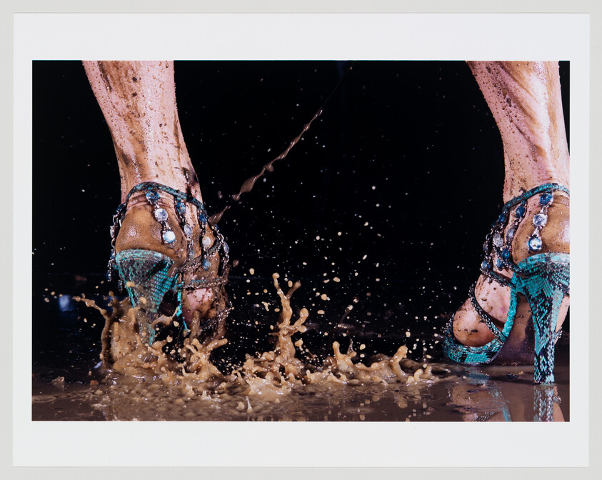 A pair of turquoise high heels splashes muddy water as a person walks through.