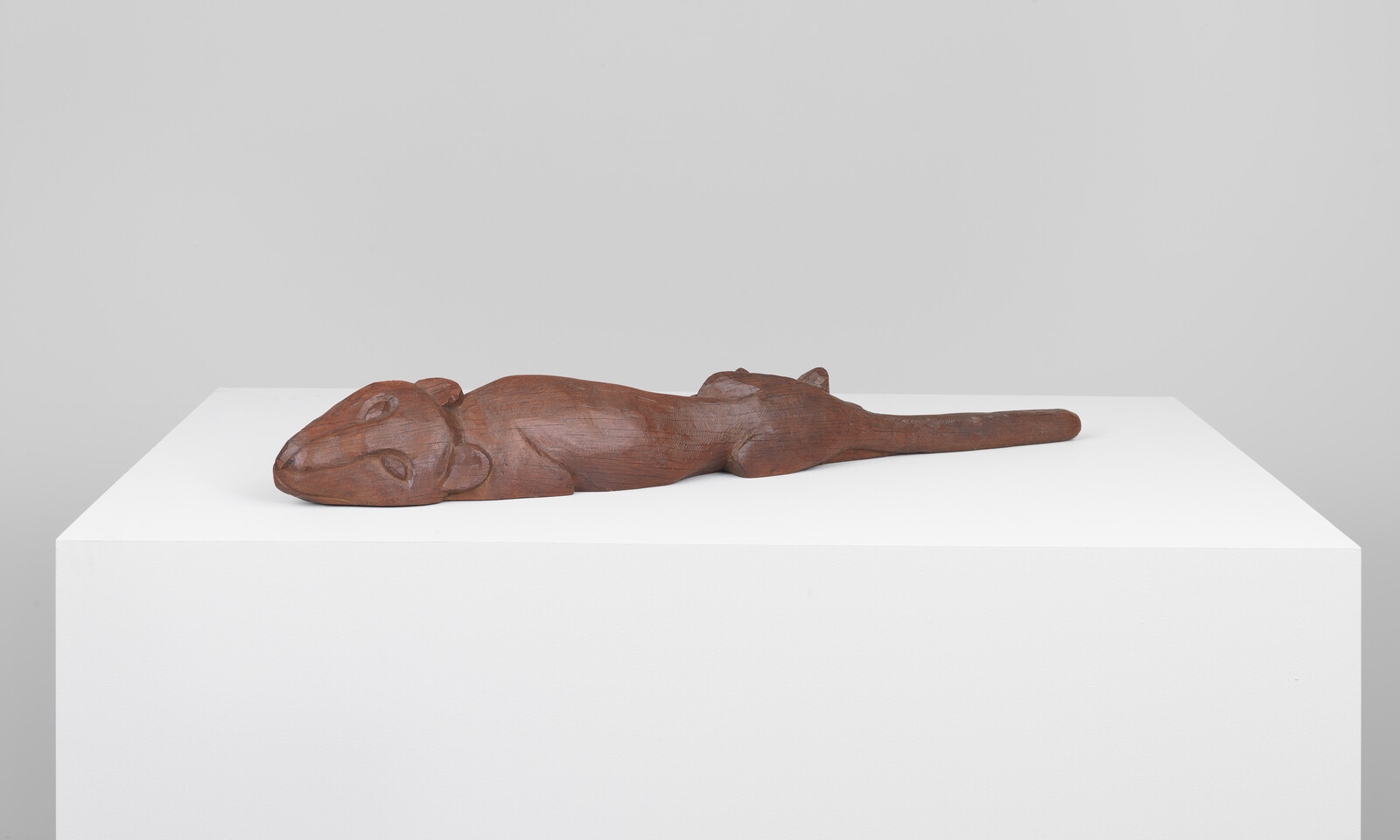 A carved wooden sculpture of a reclining animal with closed eyes and a long tail.