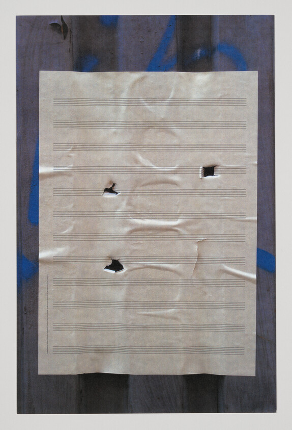 Worn music staff paper taped to wooden surface with several tears and holes.