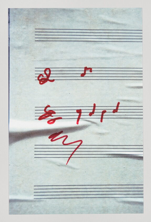 A sheet of blank staff paper with red handwritten musical notes and scribbles across creases.