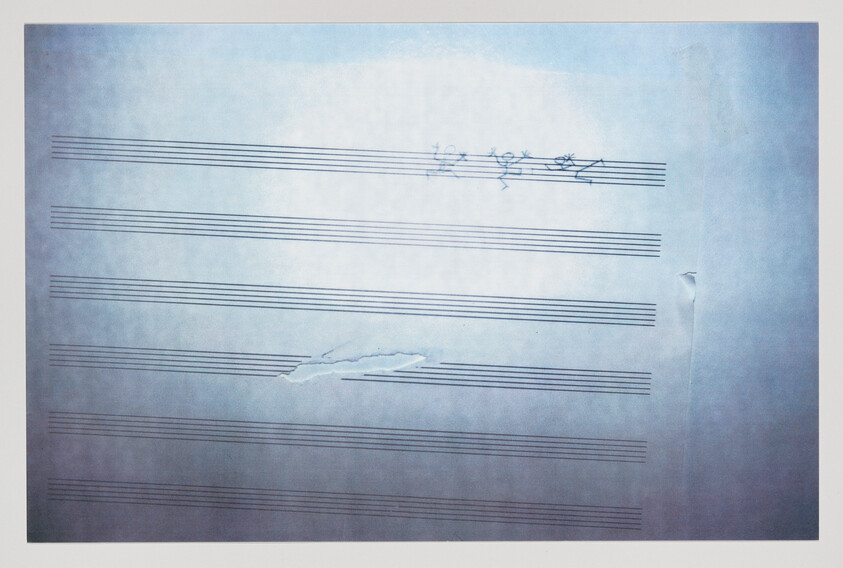 Blank sheet music paper with faint handwritten scribbles and a tear near the middle staff lines.