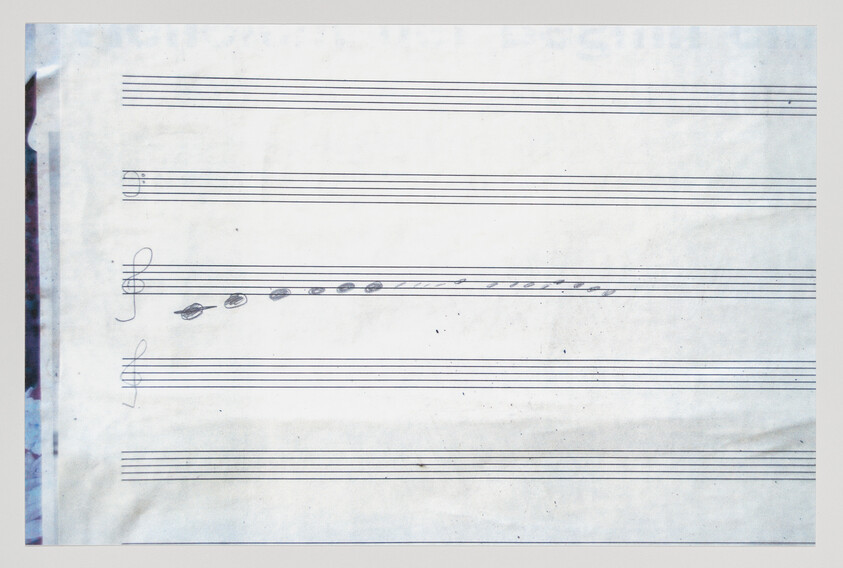 A photograph of a sheet of music paper with a few handwritten musical notes and symbols, including a treble clef and a key signature, on a stave with some visible creases and signs of wear.