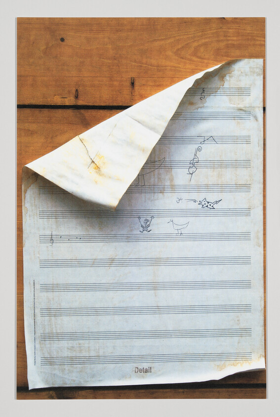 Aged music manuscript with a curled corner and small hand-drawn doodles on a wooden board.