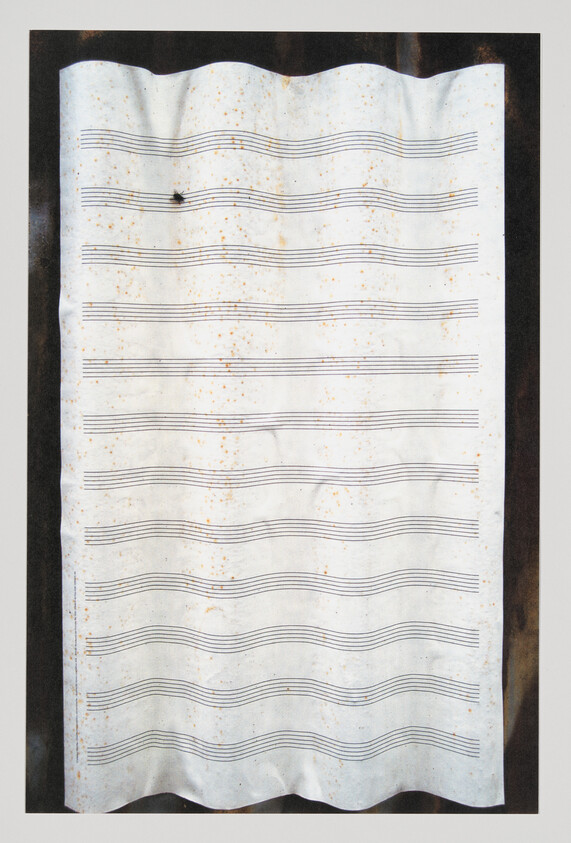 A wrinkled, stained sheet of blank music staff paper with wavy edges and a small hole.