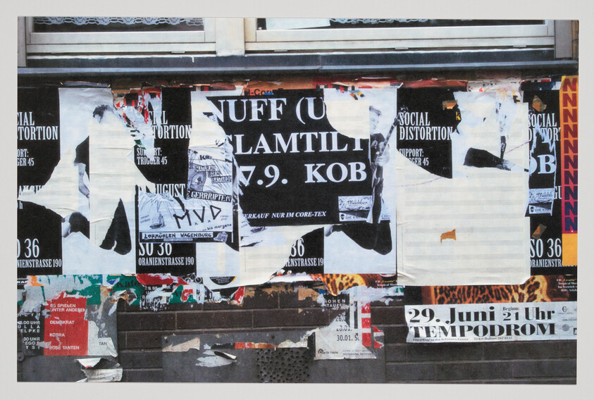 A torn poster-covered wall advertising music events and dates, with layers of paper peeling off.
