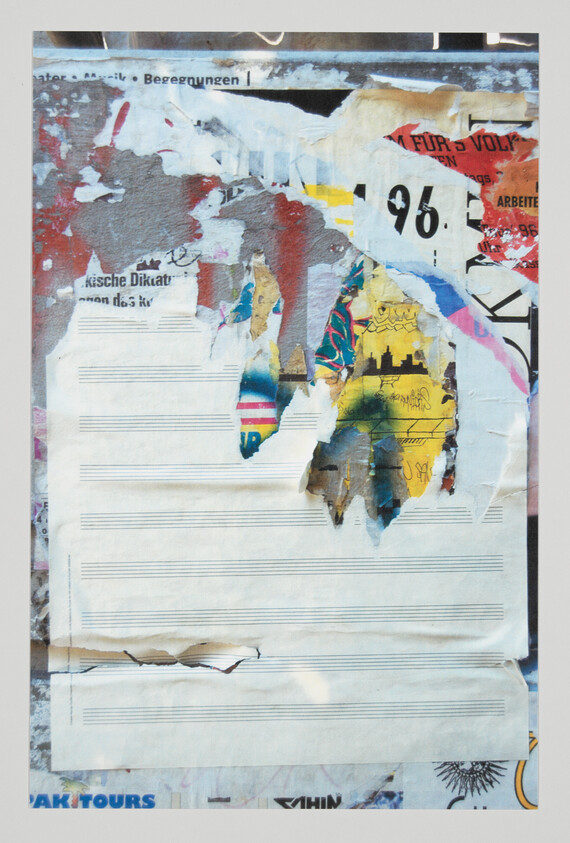 Torn layered posters reveal colorful graffiti and blank sheet music staves on a worn wall.