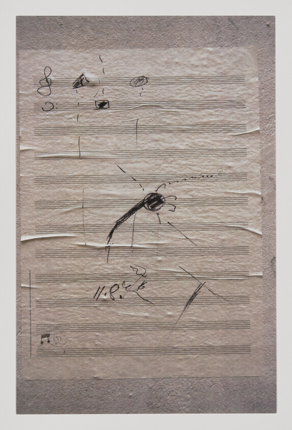 Sheet music paper with rough black ink sketches and a dark central scribble with radiating lines.