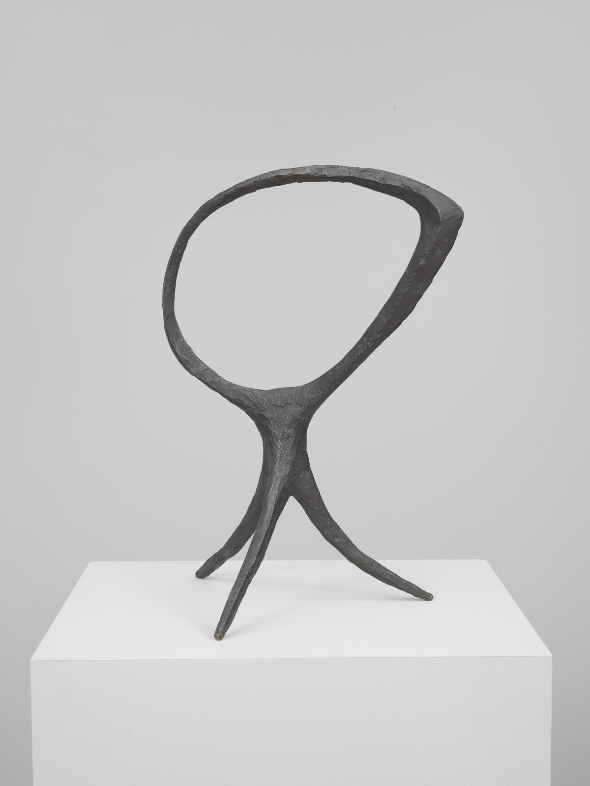Bronze abstract sculpture with an open oval top supported by three slender, tripod-like legs.