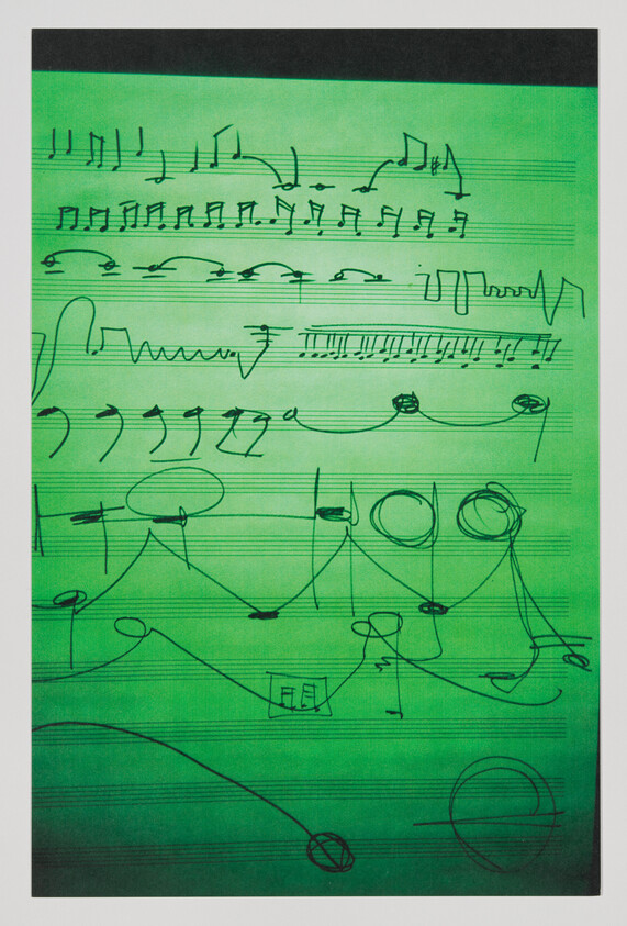 Green sheet music paper with handwritten musical notes, slurs, and abstract scribbles across staves.