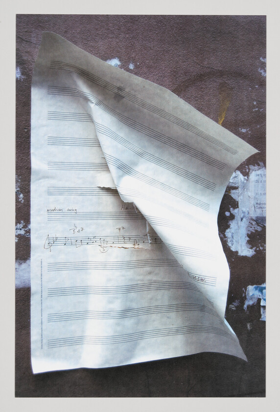 A crumpled piece of sheet music with handwritten notes and annotations lies on a textured surface with a shadowy background.