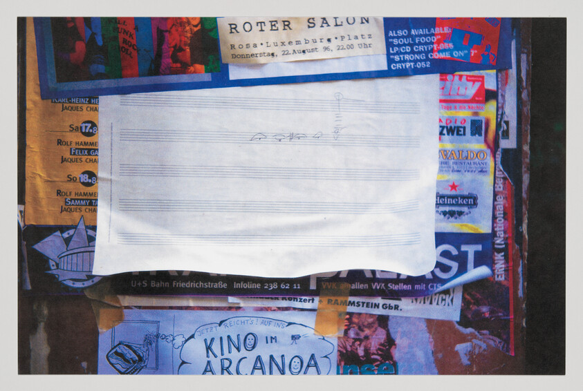Blank sheet of staff paper taped over colorful posters on a public bulletin board.