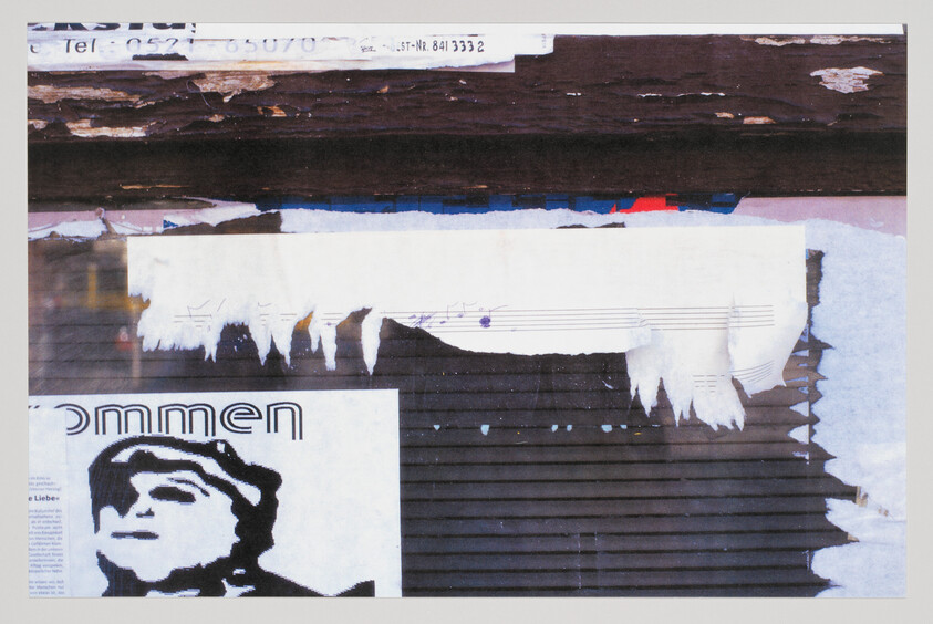 Torn posters and weathered paper strips hang on a graffiti-covered wall.