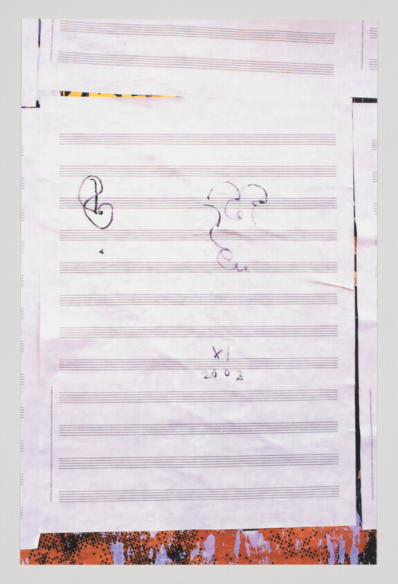 A photograph of a piece of paper with musical staff lines and a few musical symbols, including a treble clef and a bass clef, with some handwritten markings. The paper appears to be on a surface with a colorful, textured border at the bottom edge.