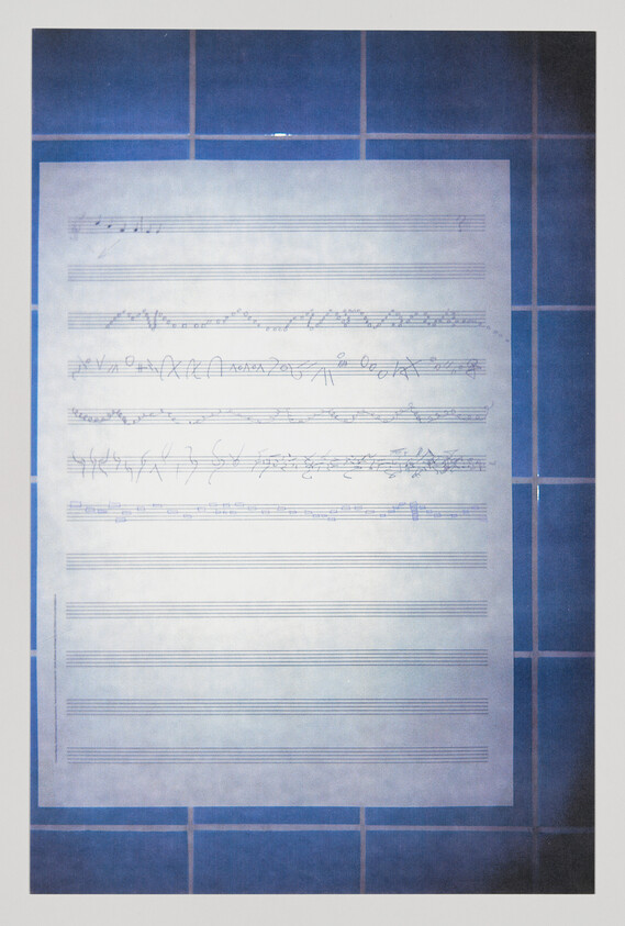 Sheet music paper with faint handwritten notes lying on a blue tiled background.