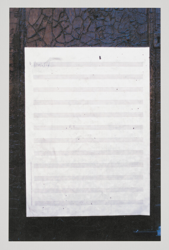 Blank sheet of music staff paper taped to a dark textured board with faint pencil marks.