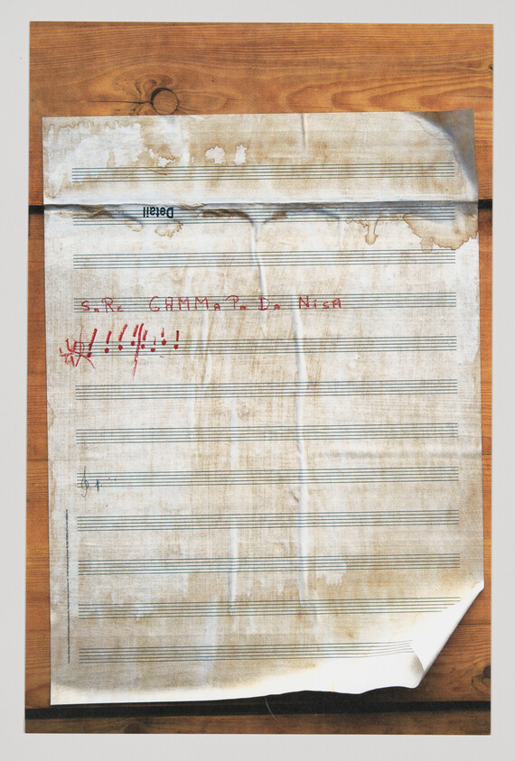 A stained, folded sheet of blank staff paper with red handwritten marks and exclamation scribbles.