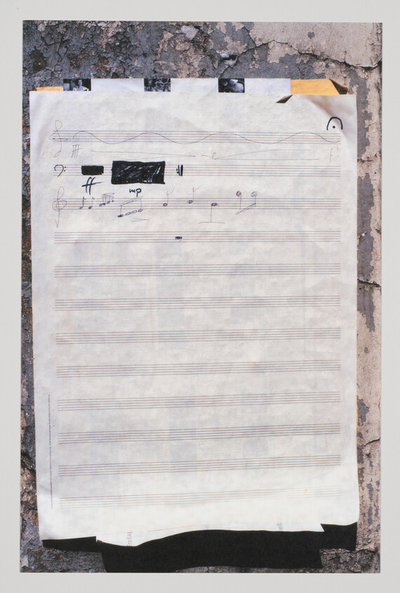 Sheet music with handwritten notes and a blacked-out section taped to a cracked wall.