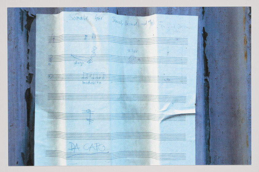 Sheet music with handwritten notes and the words "DA CAPO" taped to rusted metal.