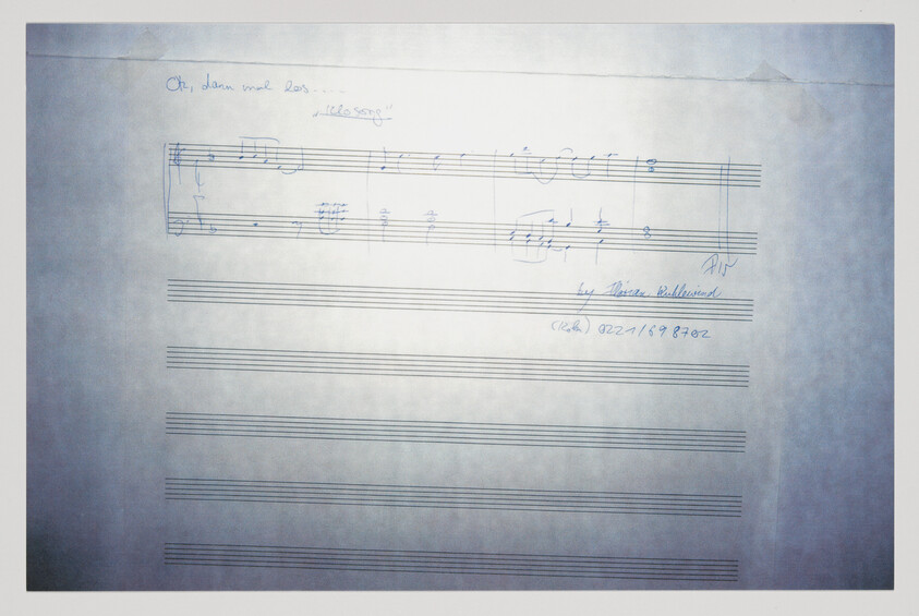 A photograph of a sheet of music paper with a handwritten musical score at the top. The title "Oh, dann mal los..." is written above the staff, and "Ideenskizze" (sketch of ideas) is noted beside it. The composer's name, Martin Behrmann, is written at the end of the musical notation, along with a date, possibly "02/21/1982". The rest of the sheet is blank, with empty staves ready for additional music notation.