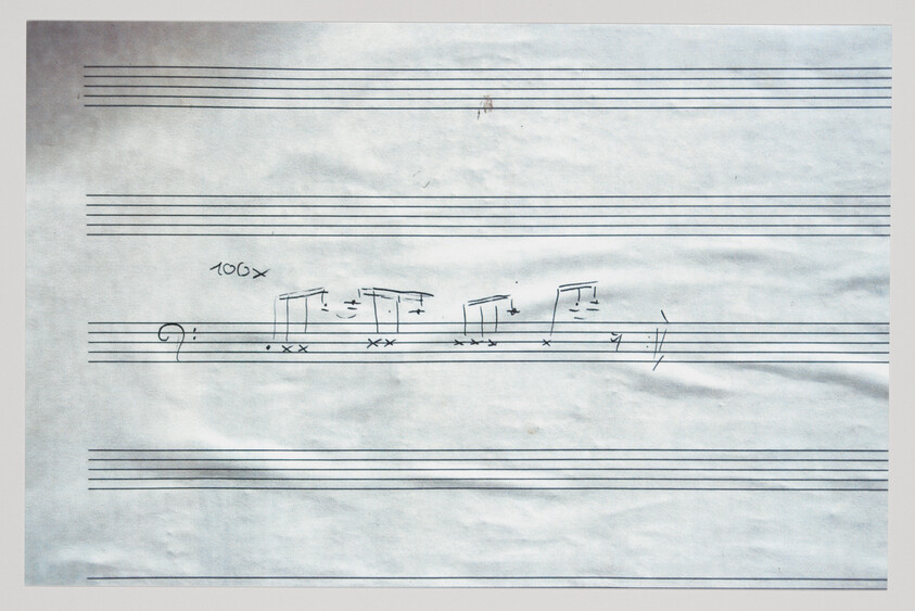 Loose sheet of staff paper with handwritten bass clef, rhythmic notes, and "100x" marking.