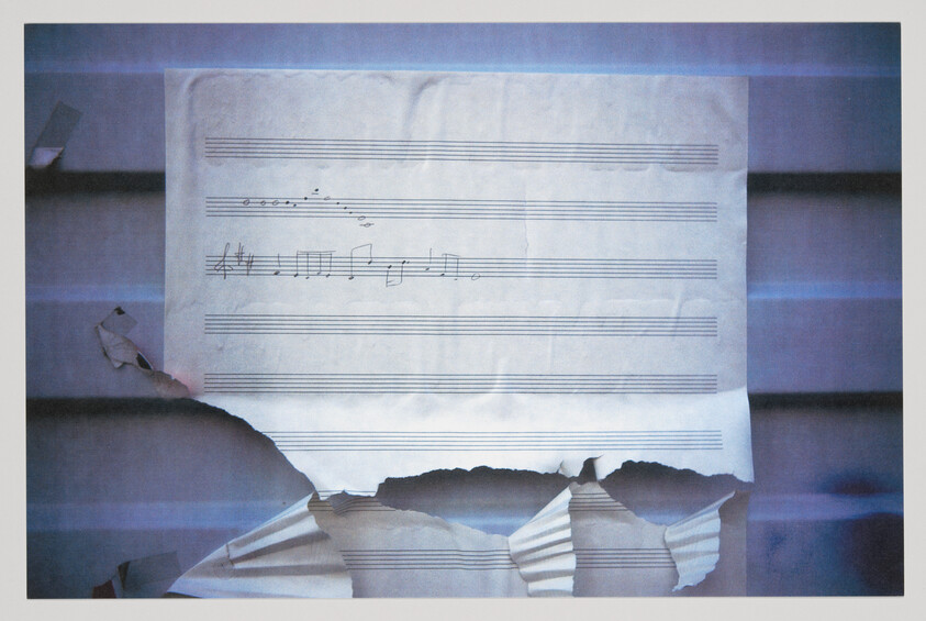 A torn sheet of blank music staff paper with a short handwritten melody taped to a wall.