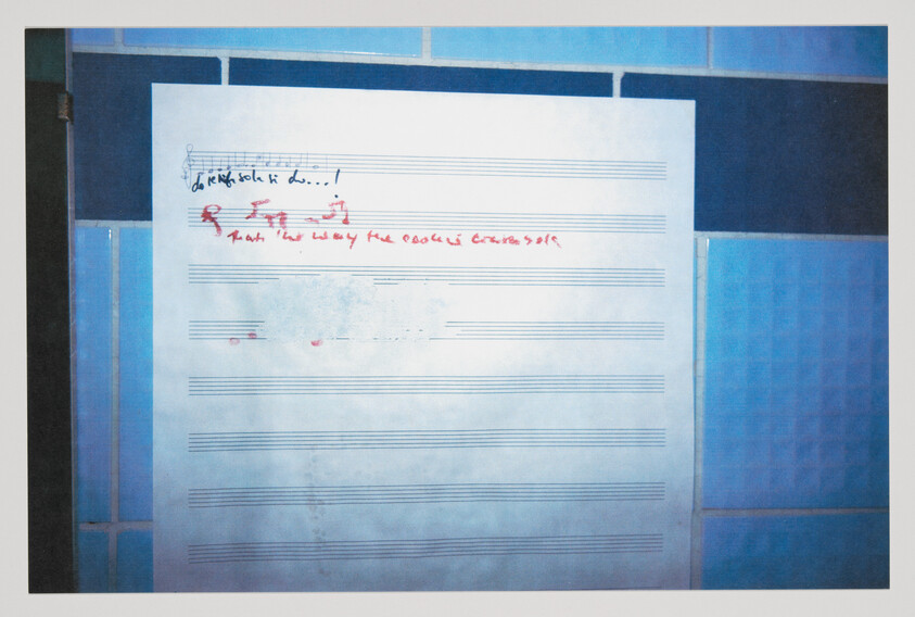 Blank sheet music with small handwritten notes and red scribbles at the top, taped to blue tiles.