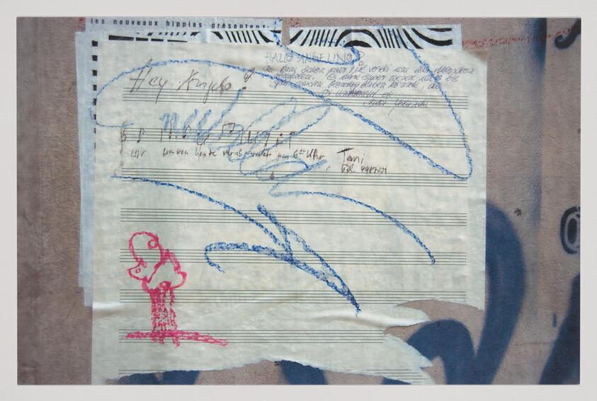 A torn sheet of music taped to a wall with blue crayon scribbles and a red doodle.