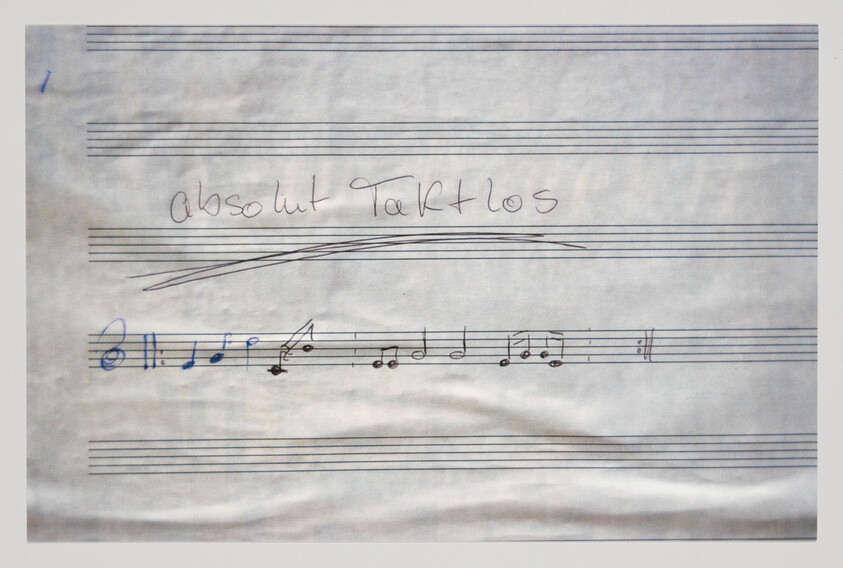 A photograph of a piece of paper with musical staff lines and handwritten musical notes. Above the staff, the words "Absolut Tarklos" are written in cursive. The paper appears slightly wrinkled.
