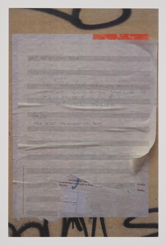 A collection of weathered papers with handwritten notes and printed text is taped to a wall with graffiti. The papers appear to be partially covering each other, and some text is obscured. The visible handwritten notes are in different handwriting styles, and there is a red tape at the top right corner of the topmost paper.