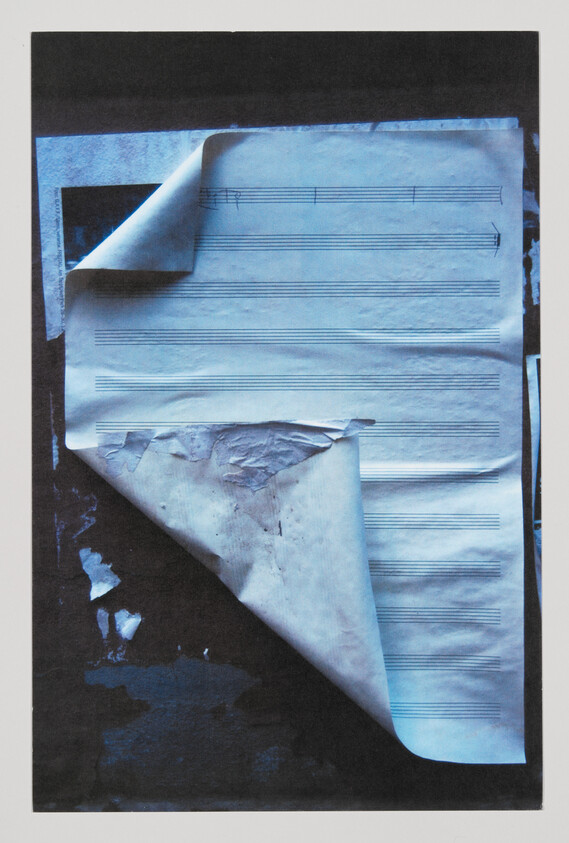 Blank sheet music with curled, peeling corners stuck to a dark textured surface.