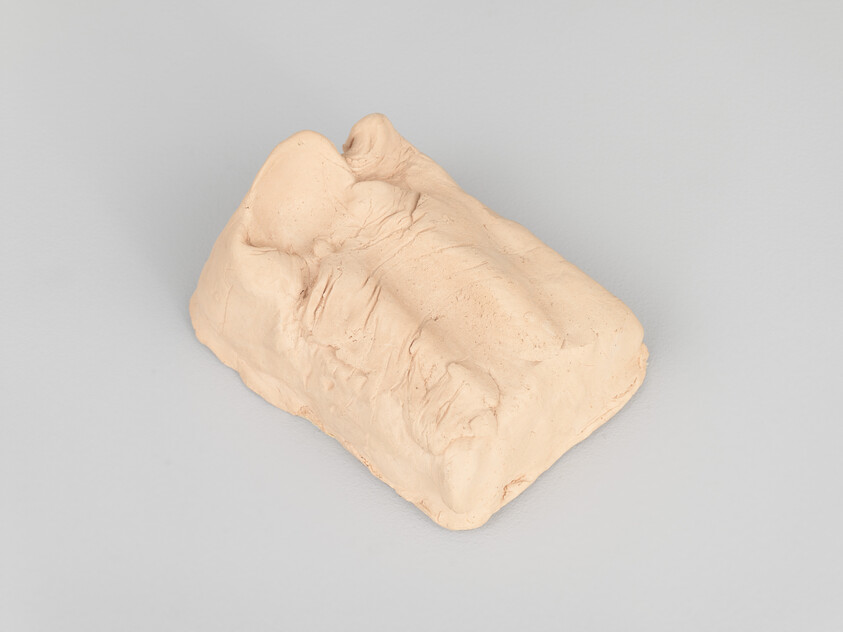 A beige piece of clay with indentations and rough textures on a gray background, resembling a partially formed sculpture or a piece of work in progress.