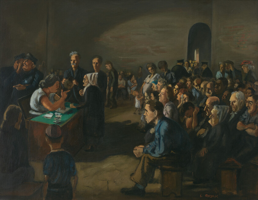 A crowded room of people waiting as a woman at a table registers or distributes papers to an elderly woman.