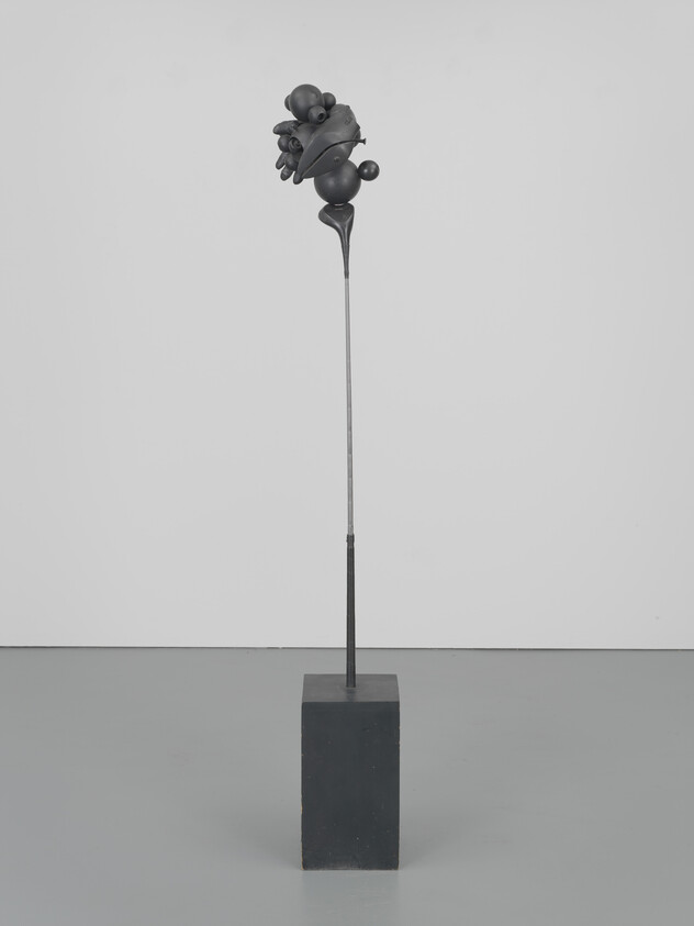 Tall thin metal sculpture on a rectangular base with an abstract clustered form at the top.