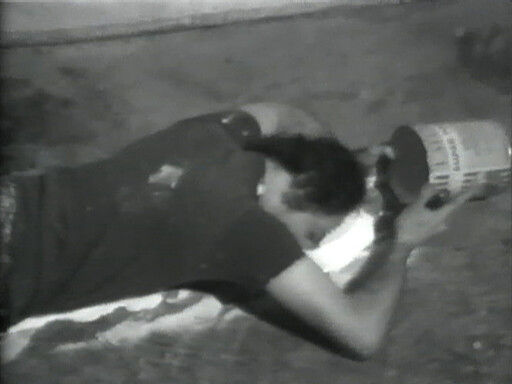 A person lies on their stomach on a bed, holding a large container near their face.