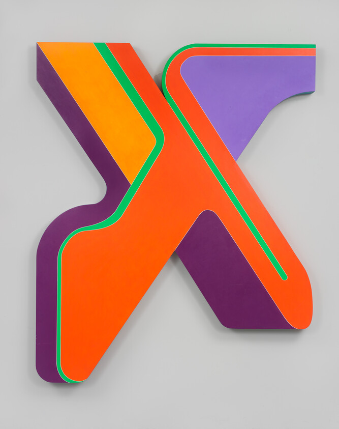 A large colorful X-shaped wall sculpture with orange, purple, green, and yellow layered panels.