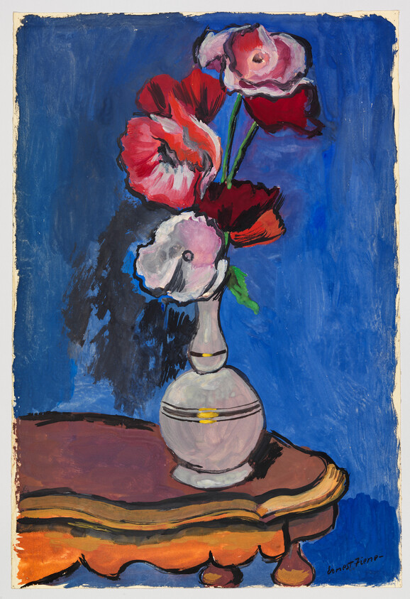 A white vase holds red and pink poppy flowers on a wooden table against a blue background.