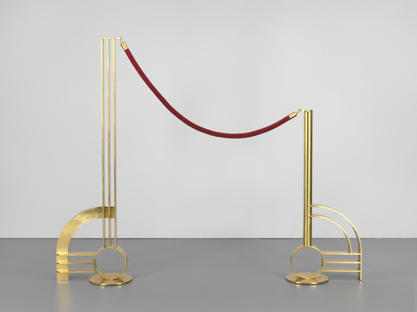 Two decorative gold stanchions connected by a red velvet rope standing on a gray floor.