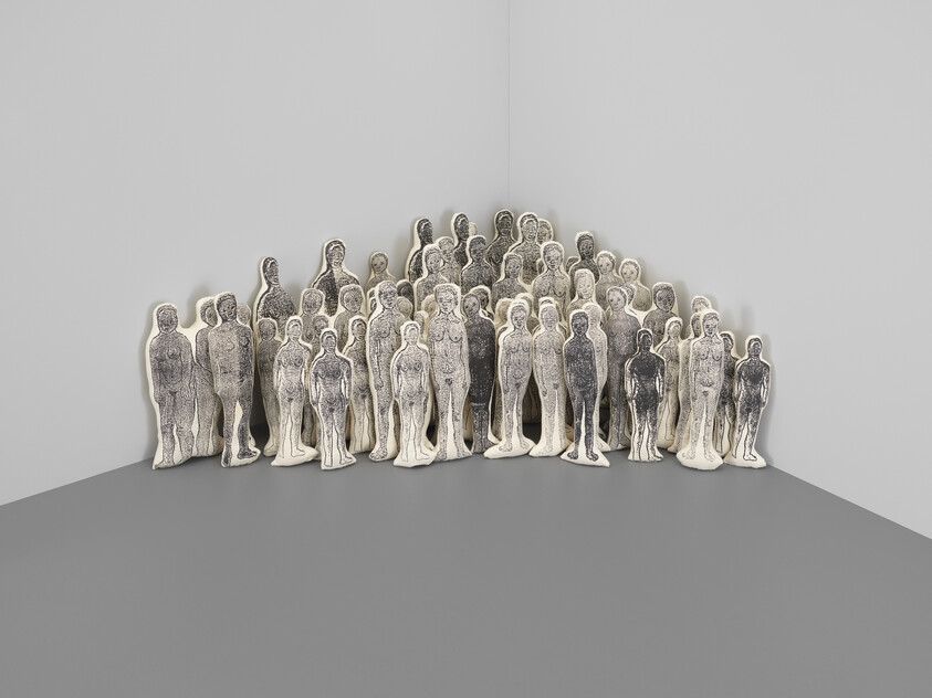 A crowd of monochrome human-shaped fabric sculptures clustered tightly in a room corner.
