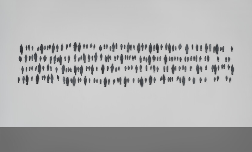 Rows of small dark leaf-shaped pieces arranged in a horizontal grid on a pale wall.