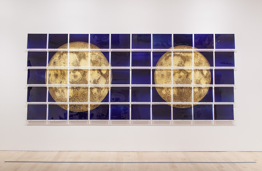 Two large golden moons are displayed on a grid of blue panels mounted on a white wall.