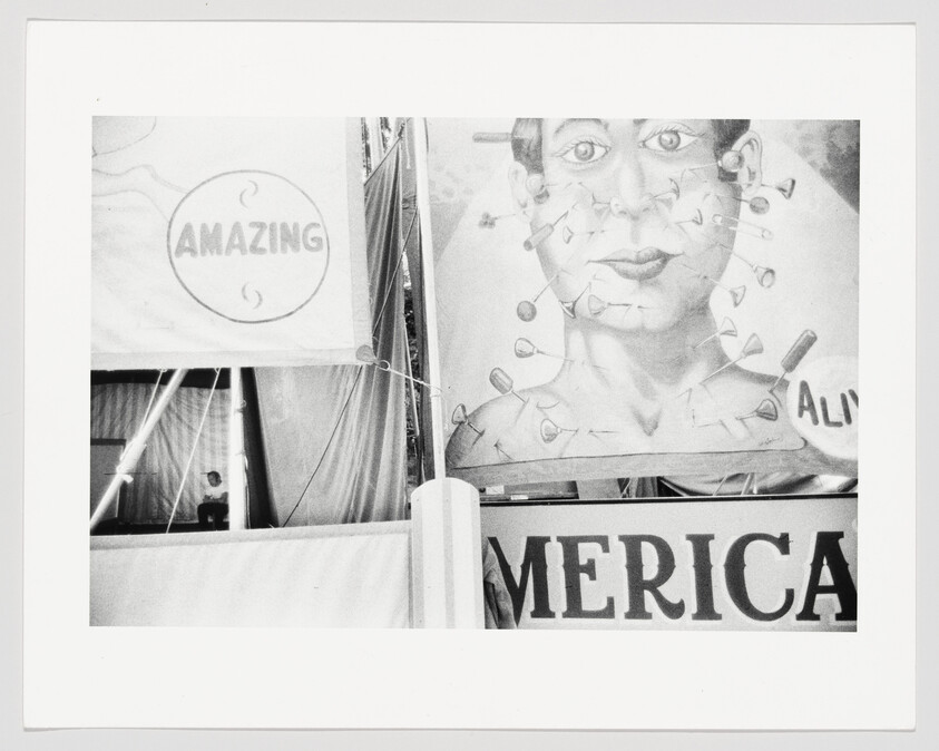 Large painted carnival banner shows a pierced face next to a sign reading "AMAZING."