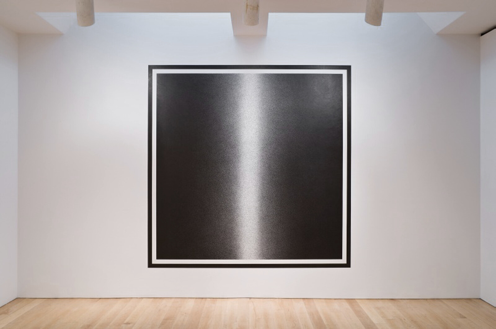 A large abstract monochrome artwork is displayed on a white wall in a gallery setting, featuring a gradient from dark to light with a vertical highlight in the center, creating an illusion of depth or a light source. The piece is framed with a thin black border and mounted at eye level, with wooden flooring extending into the foreground.