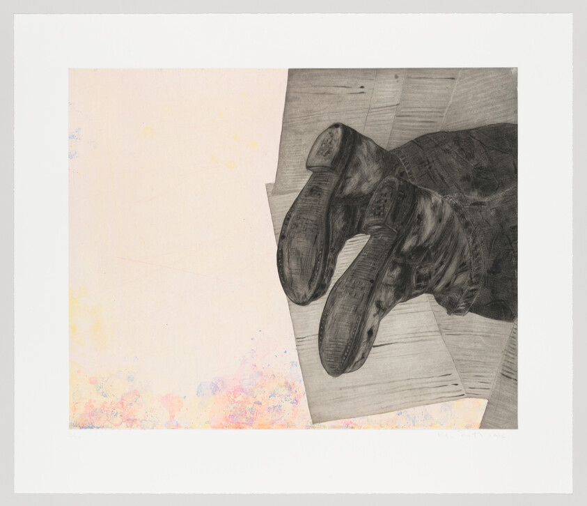 Worn black boots lying upside down on a wooden floor beside scattered papers.