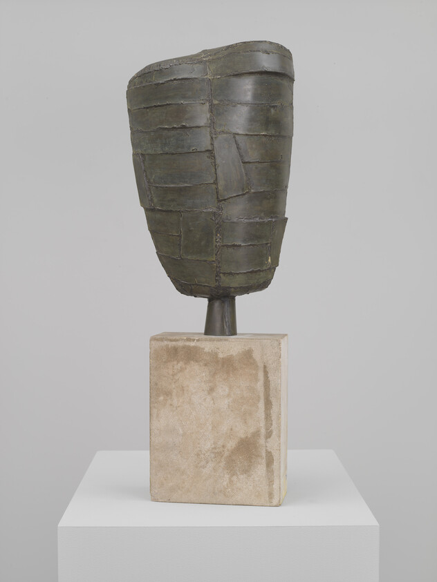 Bronze segmented abstract head sculpture mounted on a rectangular stone pedestal in a gallery.