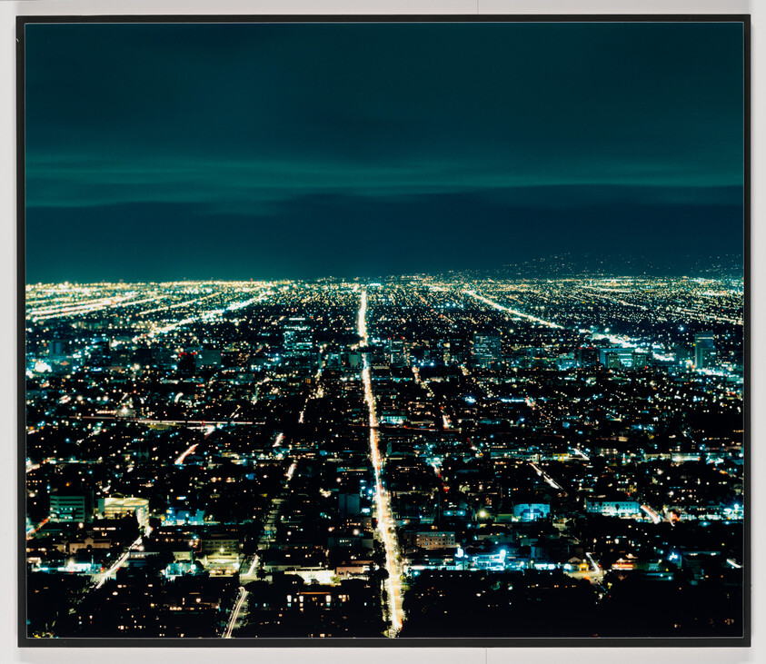 Aerial view of a city at night with a straight, brightly lit road stretching to the horizon.