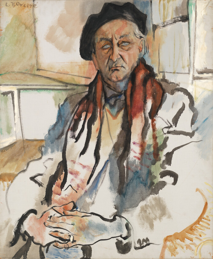 Elderly man wearing a beret and red scarf sits with hands folded, looking thoughtful.
