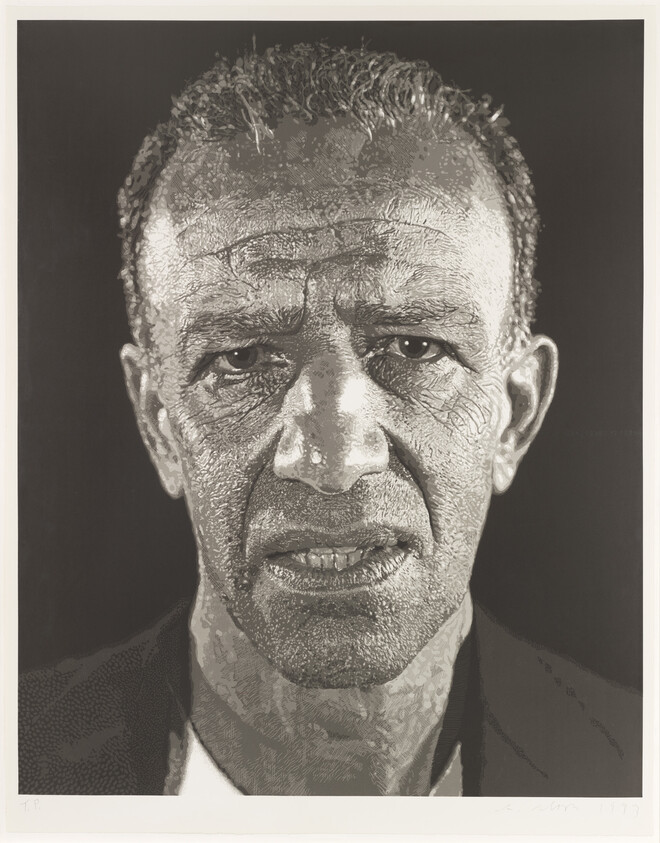 A man with short hair and a serious expression looks straight ahead, showing detailed lines and texture on his face.