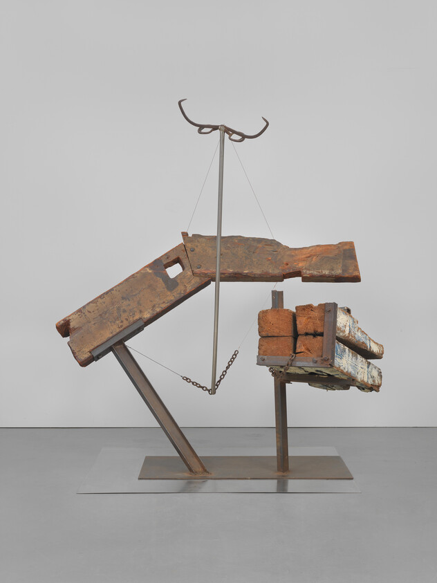 Rusty wooden and metal beams arranged and balanced on a metal stand with chains and supports.