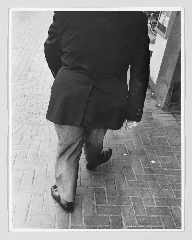 Person in a dark suit walking away on a brick sidewalk near a storefront.