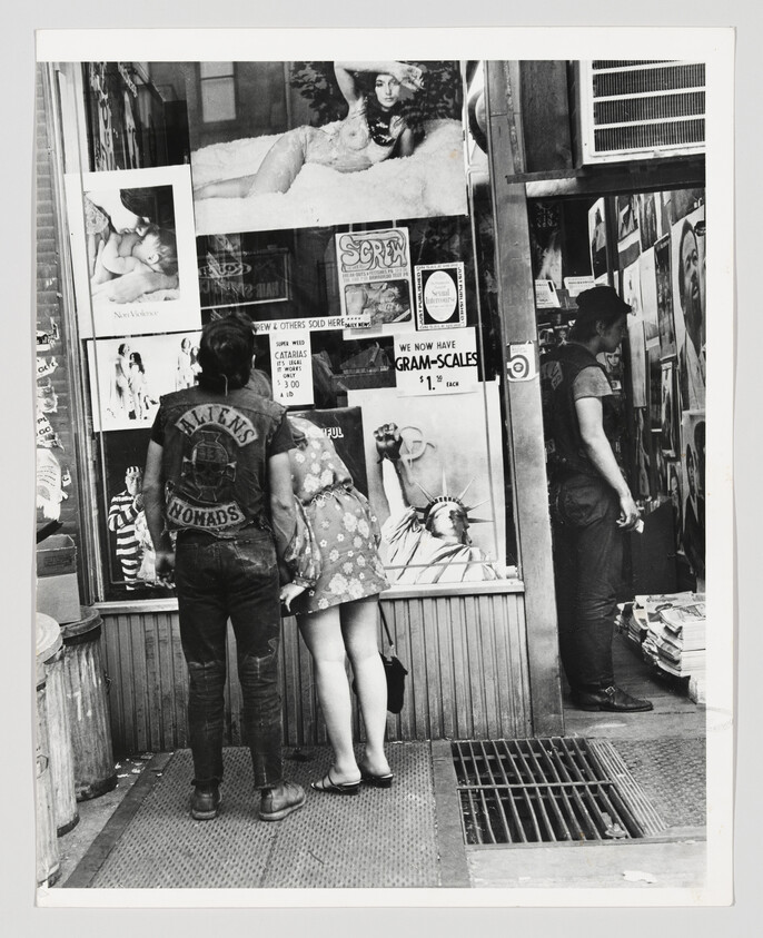 A young couple and another man peer into a magazine shop window filled with posters.